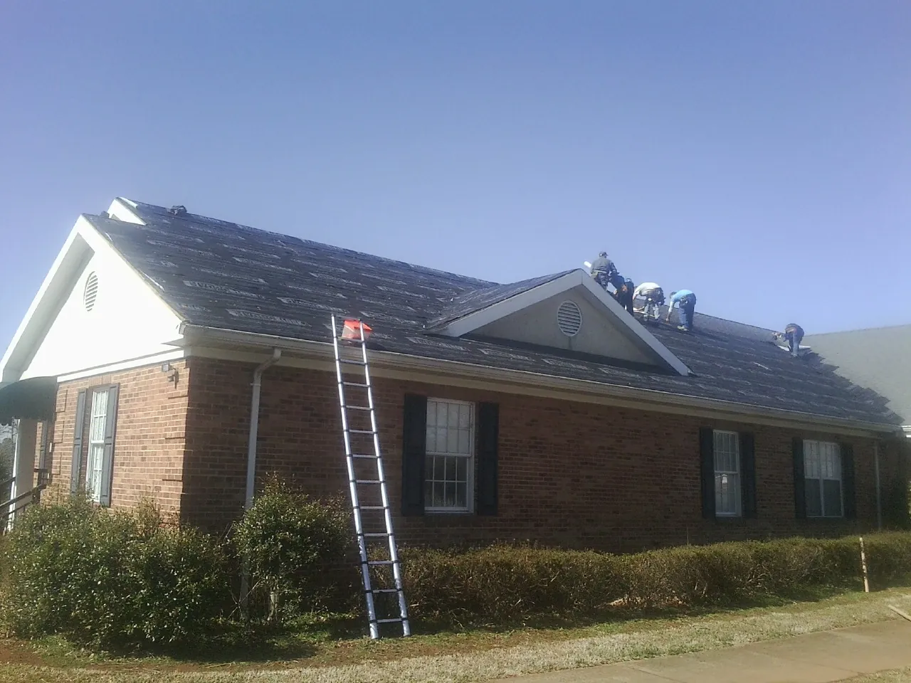 Crew tearing shingles off a brick ranch roof with a ladder set — Metal Roof Repair work by our crew in Collegedale