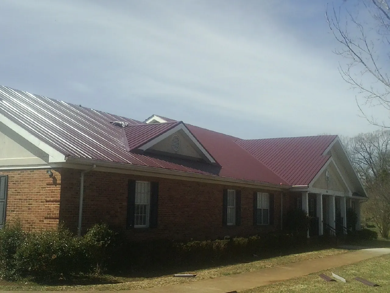 Red metal roof with gabled entries on a long brick building, from a Hail Damage Roof Repair job in Collegedale