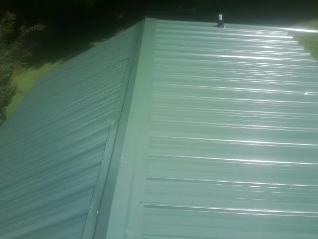 New green metal panels meeting at the ridge of a roof — Flat Roof Repair work by our crew in Collegedale