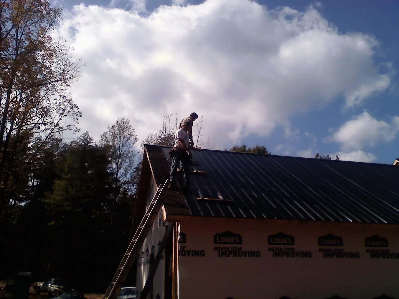 Roofer fastening dark metal panels high against a cloudy sky, from a Roof Inspection job in Collegedale
