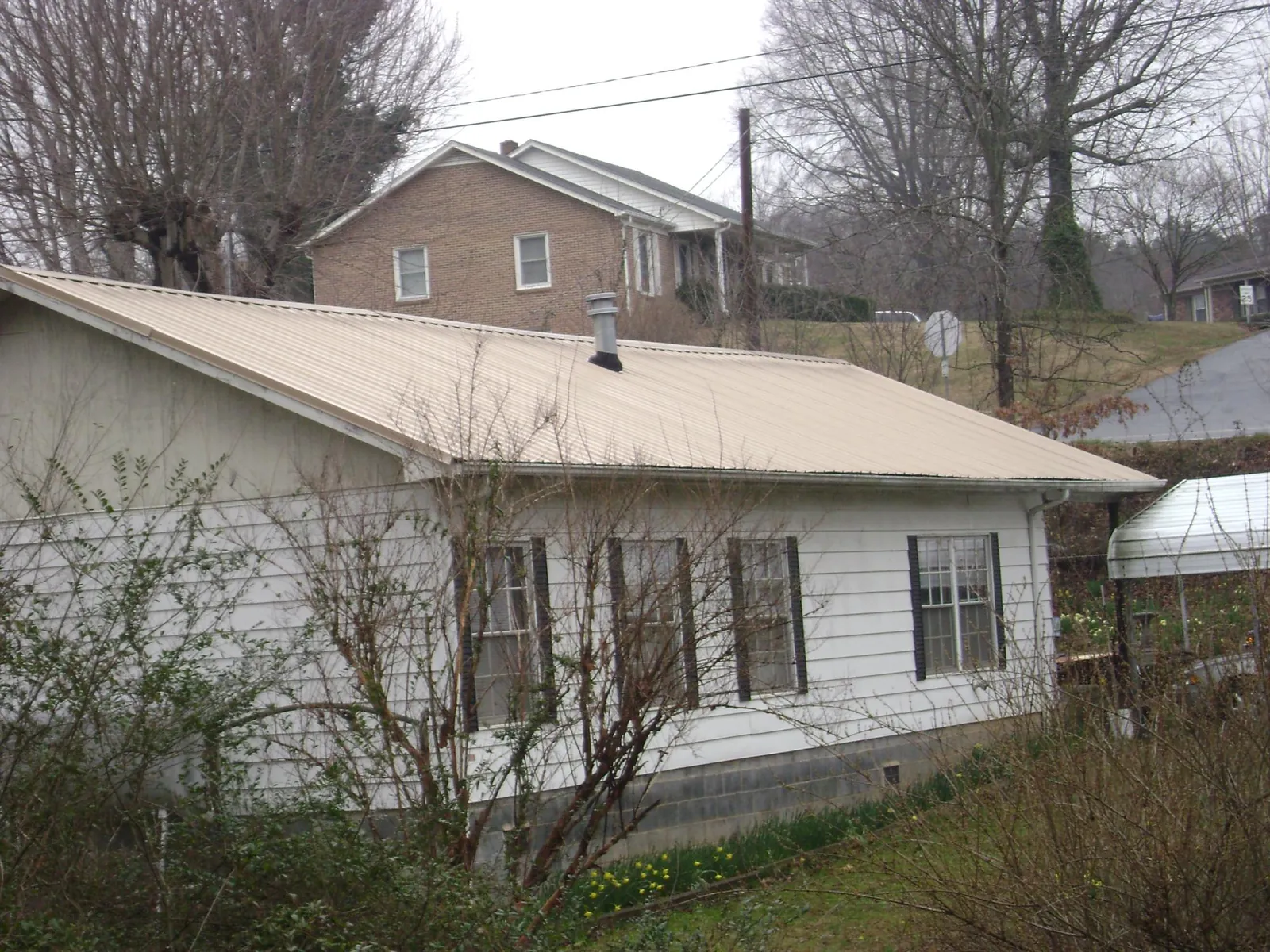 Tan metal roof on a white sided house set into a hillside — Commercial Roofing by Roofing Brothers in Collegedale
